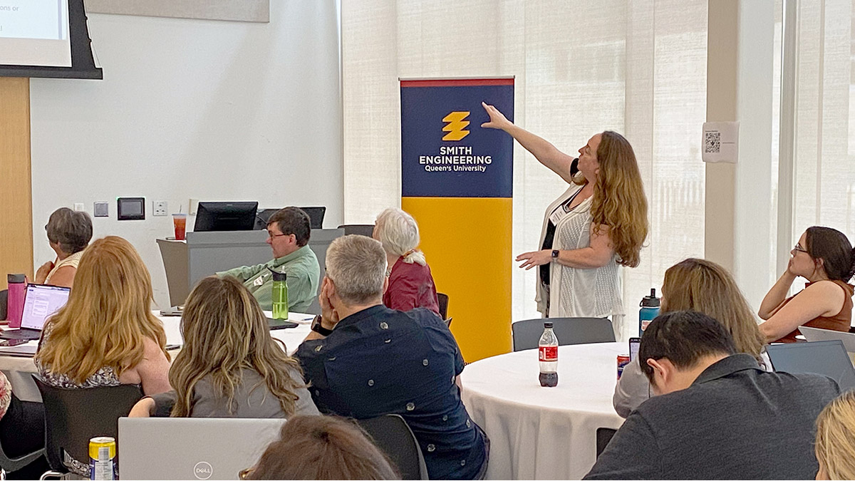 Presenter gestures toward a screen while speaking to an audience at the third annual CBA Symposium.
