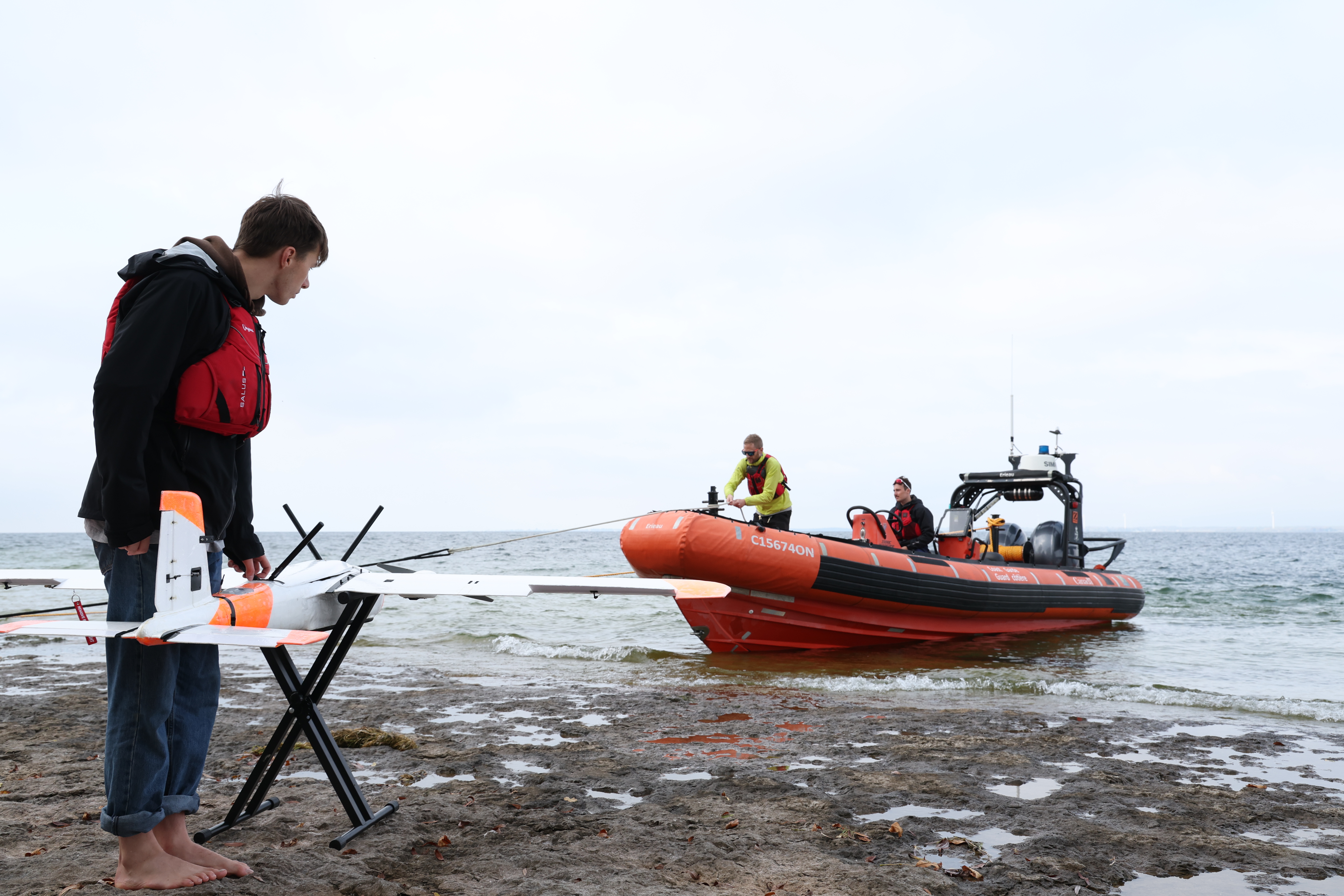 Young white man standing at a model plane. There is a dingy nearby with people in it.