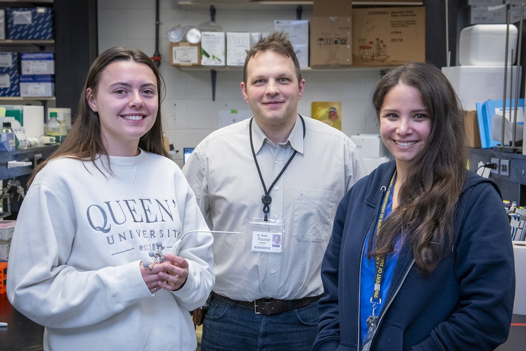 Three people are standing ina lab, looking at the camera and smiling.